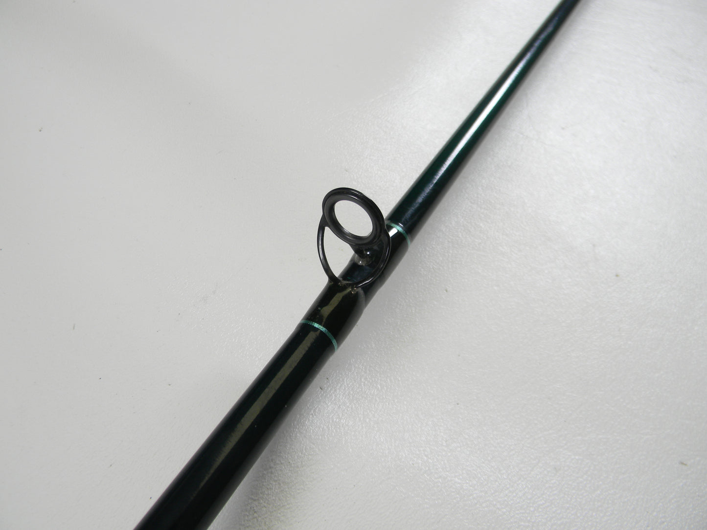A close-up of the sleek, black St. Croix Tidemaster TIC66HF 6'6" Heavy Used Casting Rod features a metallic guide ring on a light gray background. Its smooth texture makes it perfect for anglers upgrading their gear through our Trade-In Program.