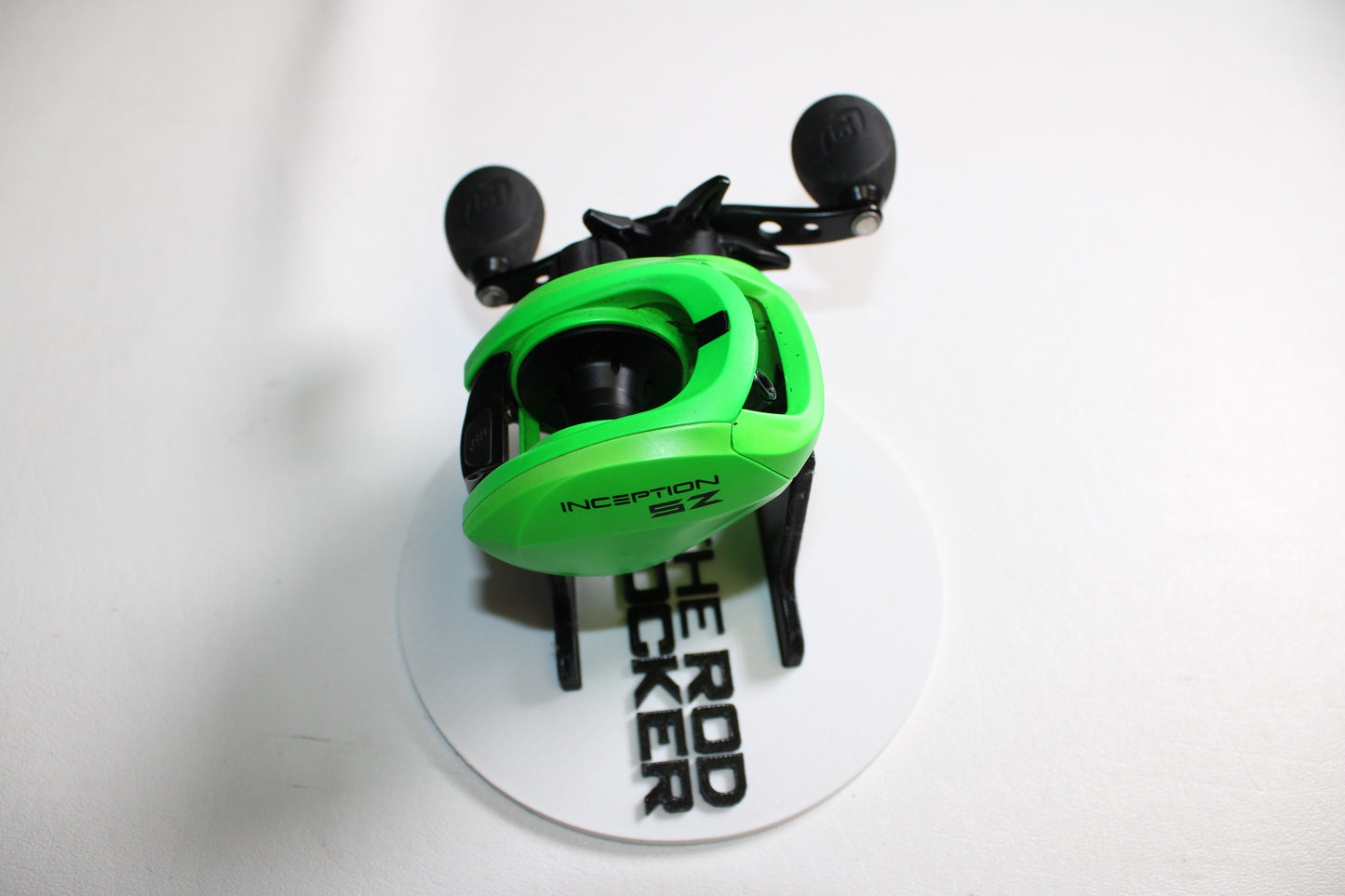 A 13 Fishing Inception Sport Z 7.3:1 Casting Reel (used, very good condition) by 13 Fishing is shown on a round white stand labeled "THE ROD DOCKER," with a plain white background.