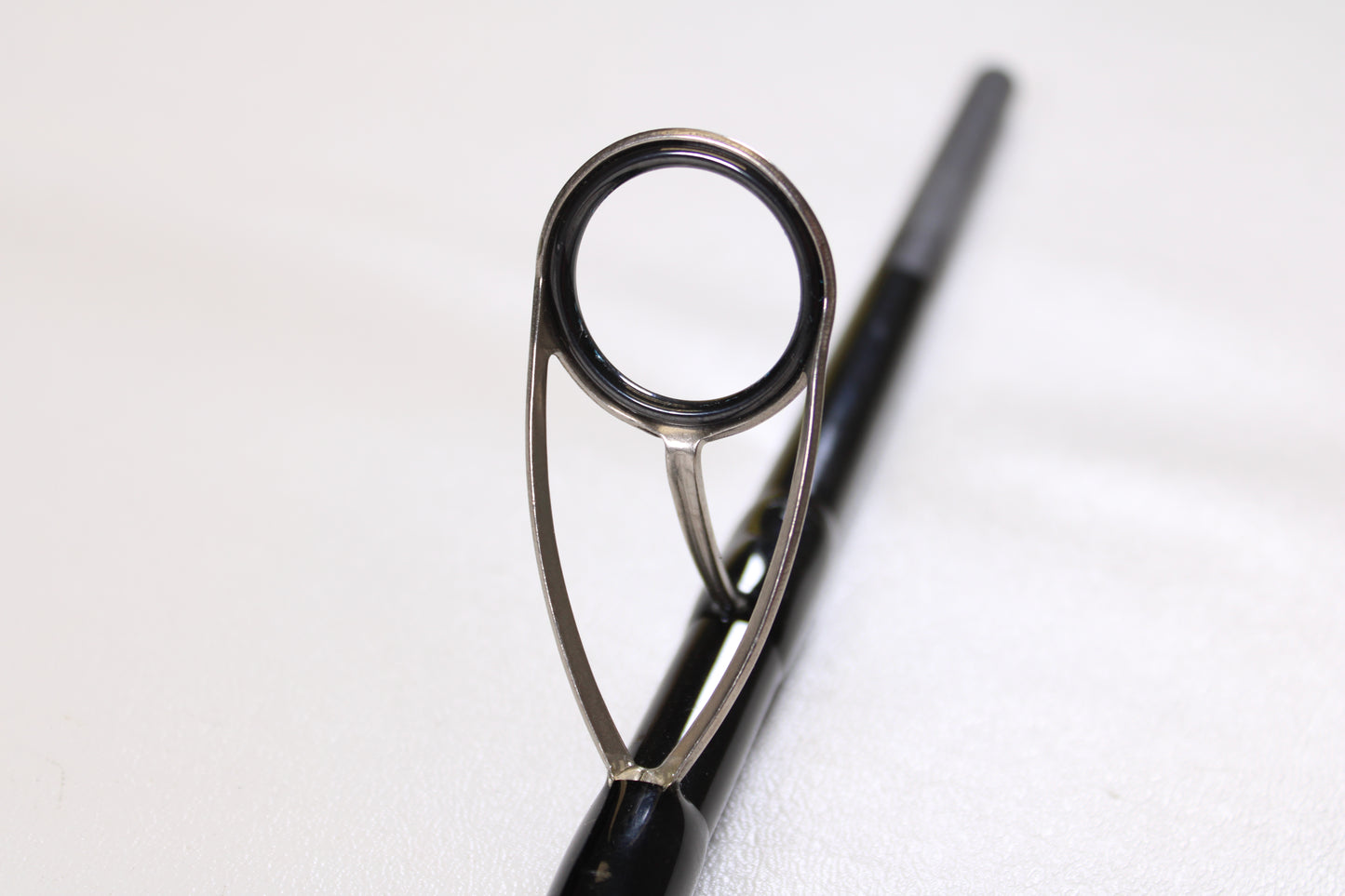 Close-up of the metal guide ring on a Century SlingShot SS 1265 10'6" 2 Piece Used Spinning Rod in excellent condition, with the rod extending out of focus—ideal for highlighting quality gear in our Century trade-ins.