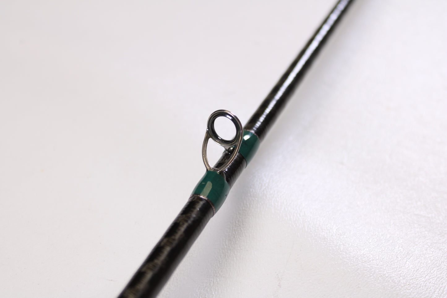 Close-up of a G. Loomis Conquest CNQ 783C MBR 6'6" Medium Heavy Used Casting Rod in excellent condition, featuring a metal guide ring with green thread, perfect for our Rod and Reel Trade-In Program. Shown on a plain white background.