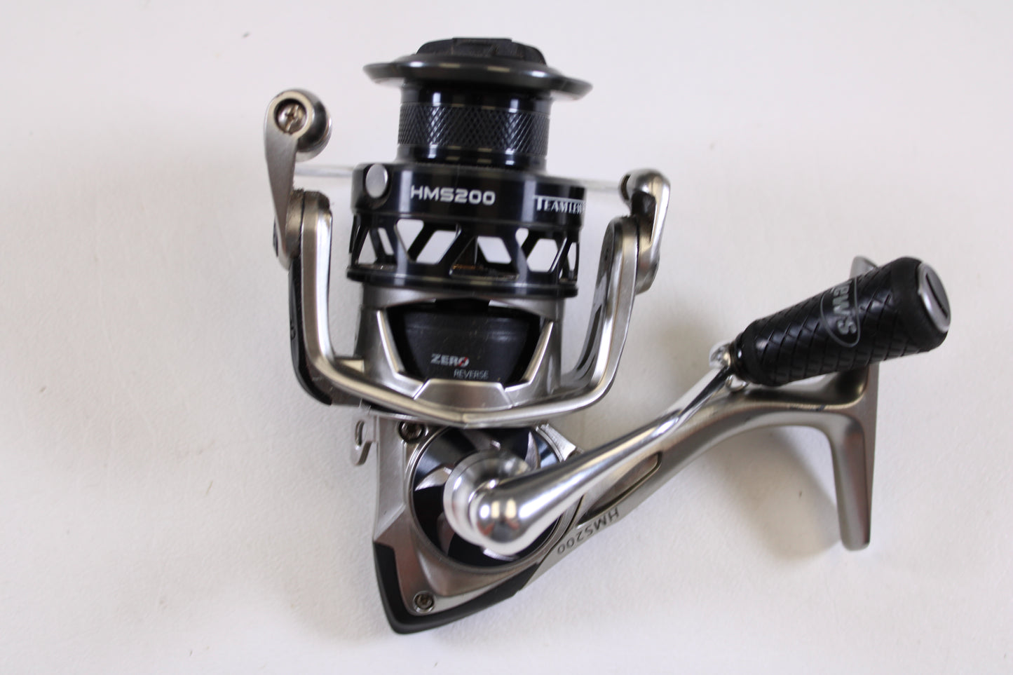 A close-up of a Lew's HyperMag HMS200 6.2:1 used spinning reel in fair condition (missing handle nut) is displayed on a white surface—ideal for upgrading via our rod and reel trade-in program for store credit on used gear.