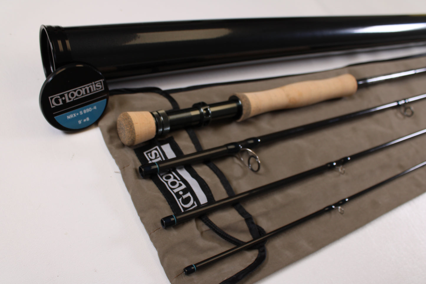 The G. Loomis NRX+ S 890-4 Used Fly Rod (Mint Condition) is shown disassembled with four segments, a cork handle, protective sleeve, and black carrying tube—all branded by G. Loomis—displayed on a white surface.