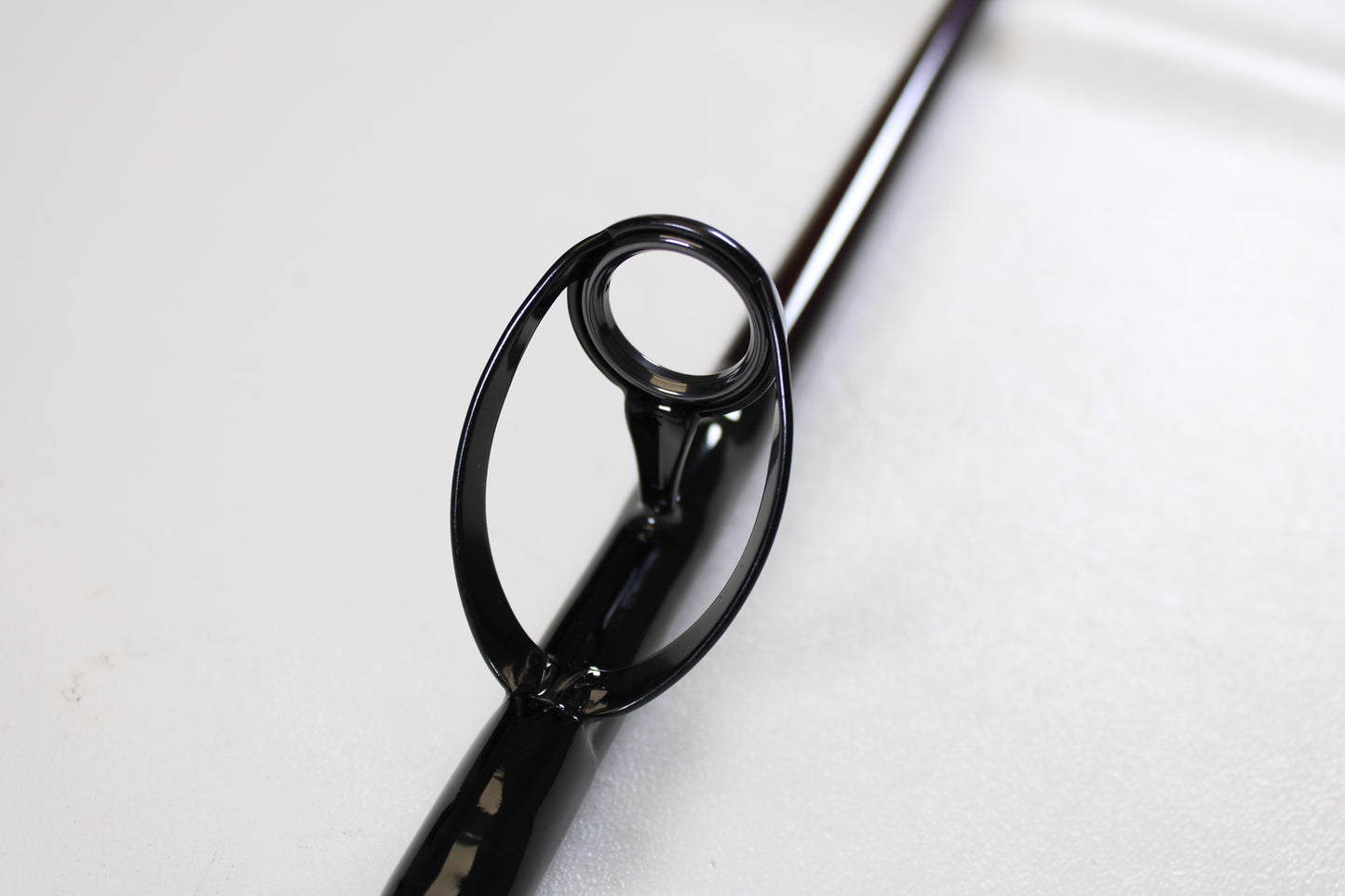 Close-up of a St. Croix Mojo Salt MSWC76MHMF 7'6" Medium Heavy used casting rod guide on a smooth, light surface. This mint condition rod is ideal for anglers trading in gear for store credit with our Rod and Reel Trade-In Program.