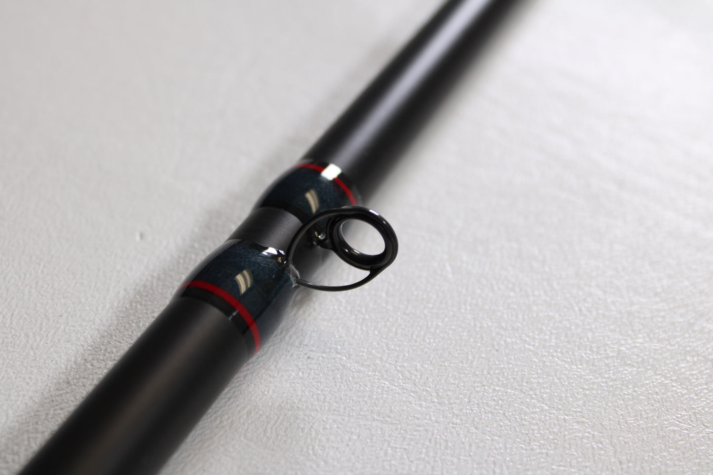 Close-up of the Falcon Slab Series SLS13MH 13'0" Medium Heavy 3pc Used Spinning Rod in excellent condition, with black finish, metal guide ring, and red-silver accents—ideal for used gear buyers or our rod and reel trade-in program.