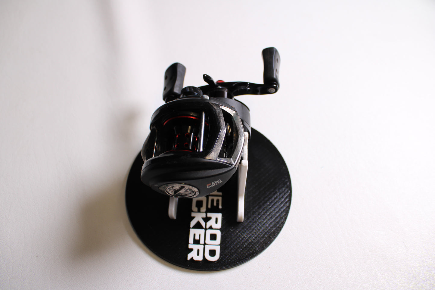 An Abu Garcia Revo 3 SX-L casting reel in good condition rests on a round black mat labeled "ROD LOCKER," all placed on a white surface.
