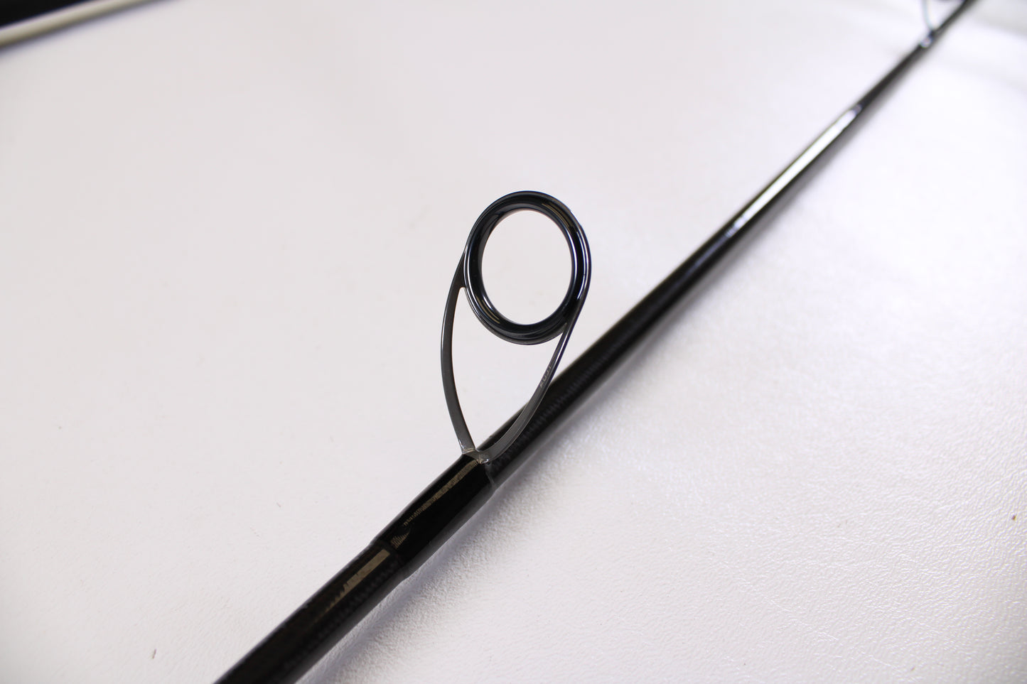 Close-up of an ODM Rods Genesis Surf NGX-802 8'0" used spinning rod guide on a white surface—excellent condition. Trade in your used gear like this through our Rod and Reel Trade-In Program for store credit.