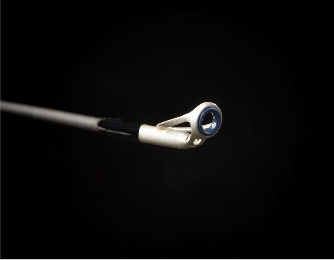 Close-up of the Falcon Cara Casting Rod Eye Crosser 6'11" Heavy (CC-7-1611) metallic guide with a blue ring, set against a black background, showcasing premium Fuji components and carbon fiber construction.