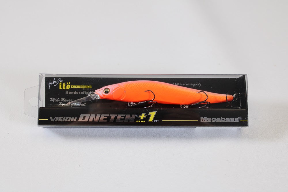A bright orange Megabass ITO Vision 110+1 (SP-C) Secret V-Ore jerkbait fishing lure is displayed in clear packaging labeled with “VISION ONETEN +1” and bold black and yellow Megabass branding.