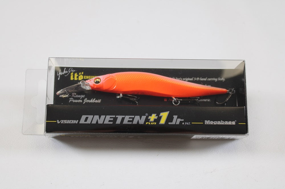 The Megabass Vision 110+1 Jr. Jerkbait (SP-C) Secret V-Ore, a vibrant orange lure by Megabass, comes in a clear plastic box with black and yellow text—ideal for bass fishing fans.