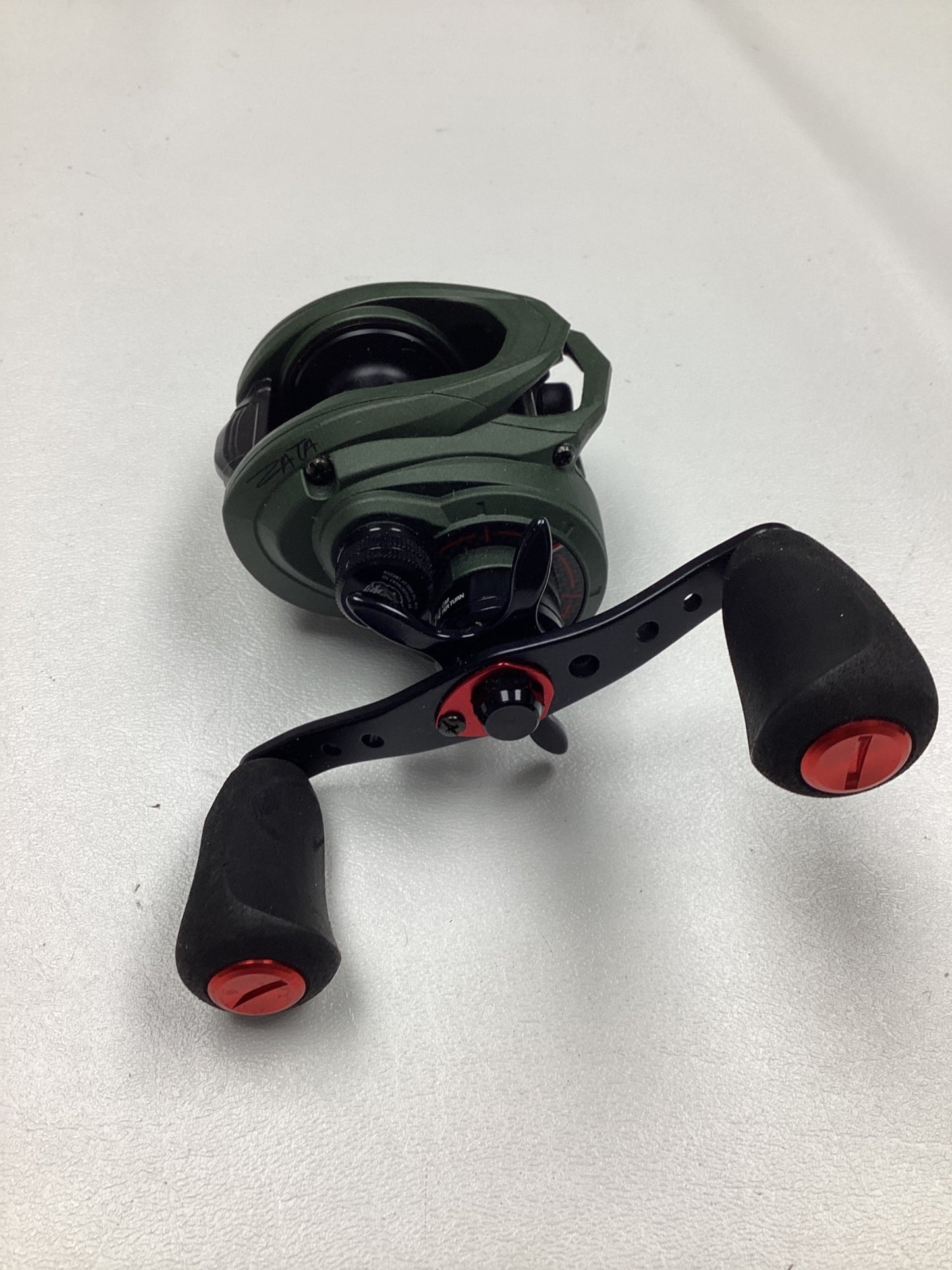 Abu Garcia Zata 7.1:1 right-hand baitcasting reel in green and black with two large black handles with red caps, excellent used condition, shown on a plain white surface.