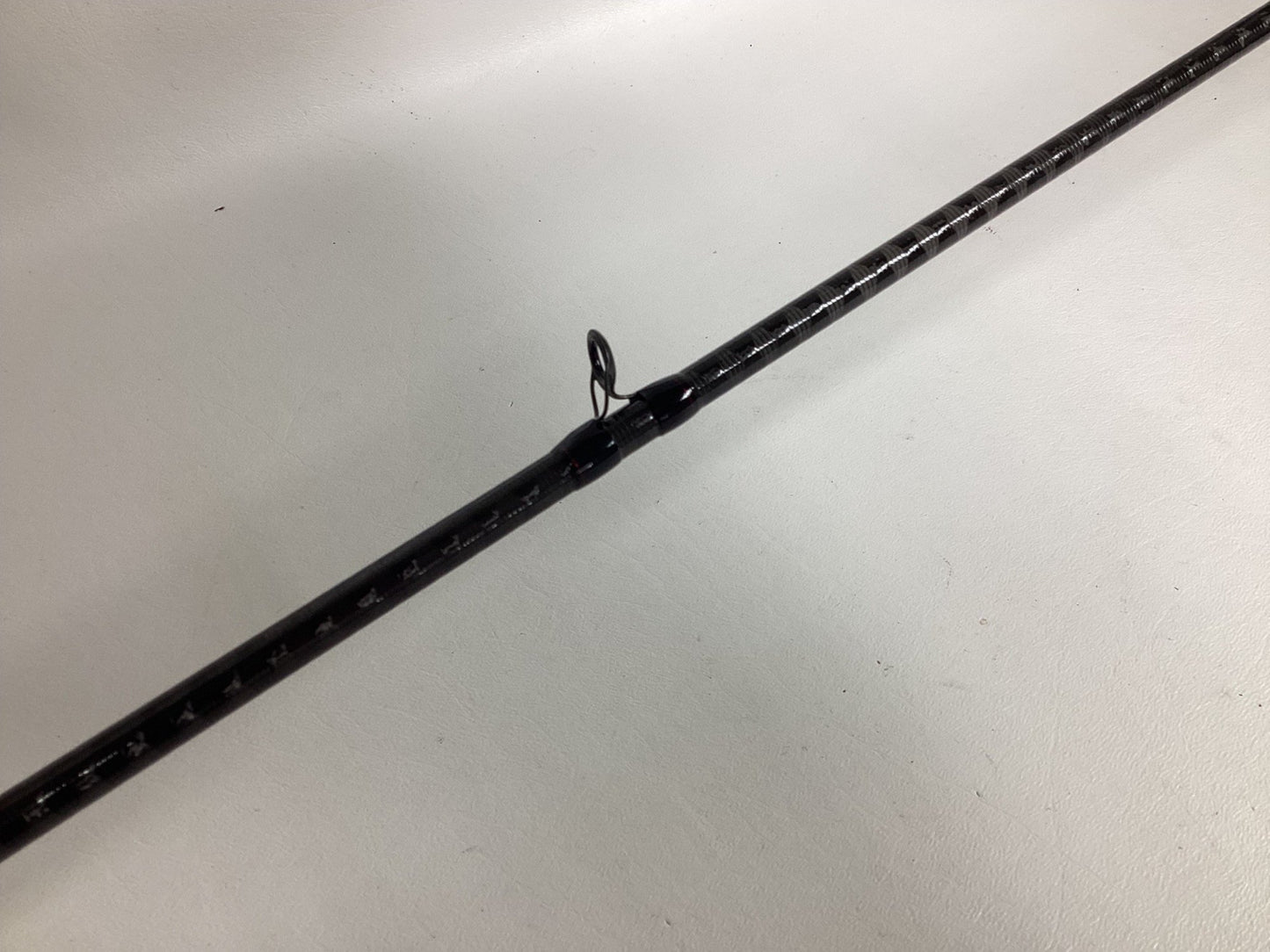 Close-up of a Shimano Zodias ZDC610MHA black fishing rod on a white background, featuring a line guide ring at the center, textured surface, and white markings. Trade it in through the Nation's Best Rod and Reel Trade-In Program for store credit.