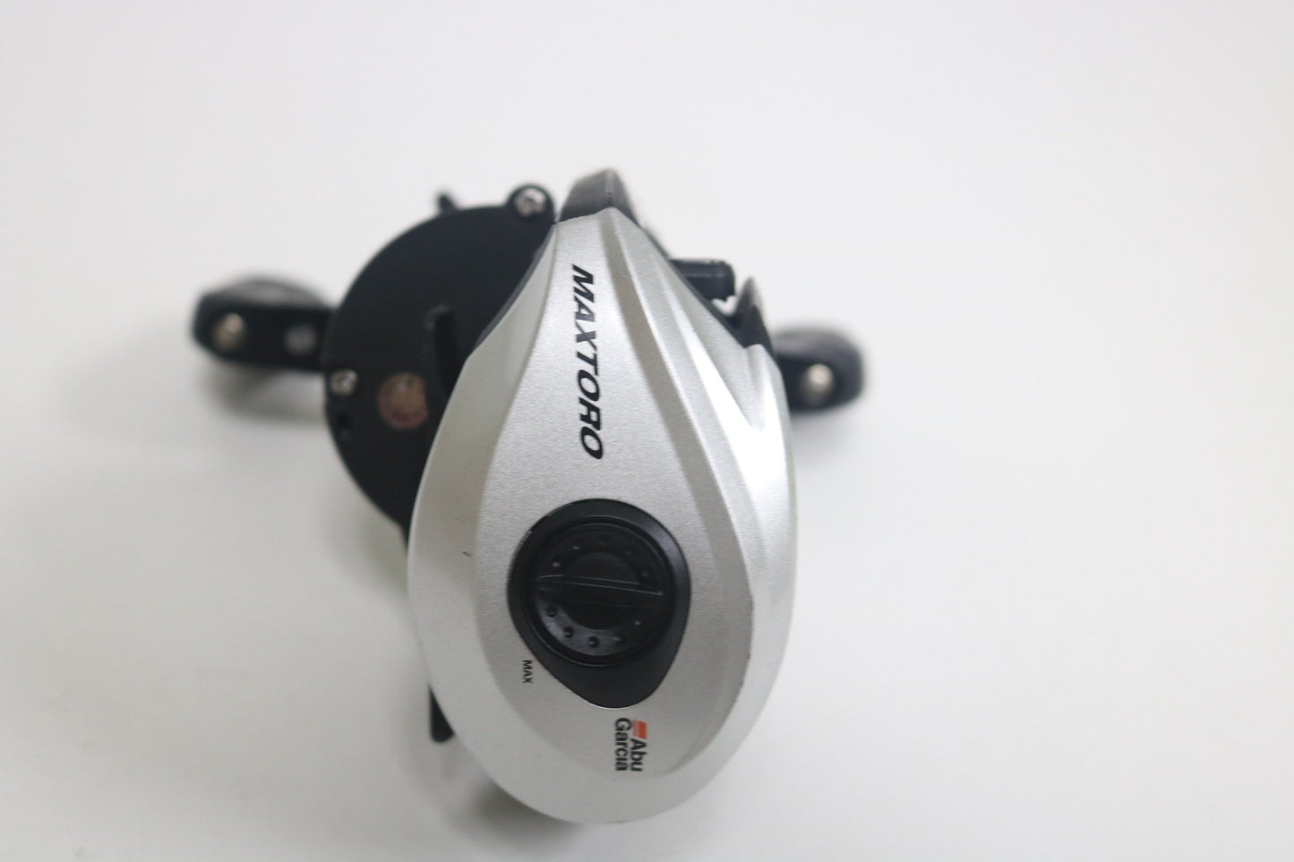A silver and black Abu Garcia MAXTORO 5.3:1 baitcasting reel in very good used condition is shown on a white background, featuring an adjustment dial and the brand logo near the bottom.