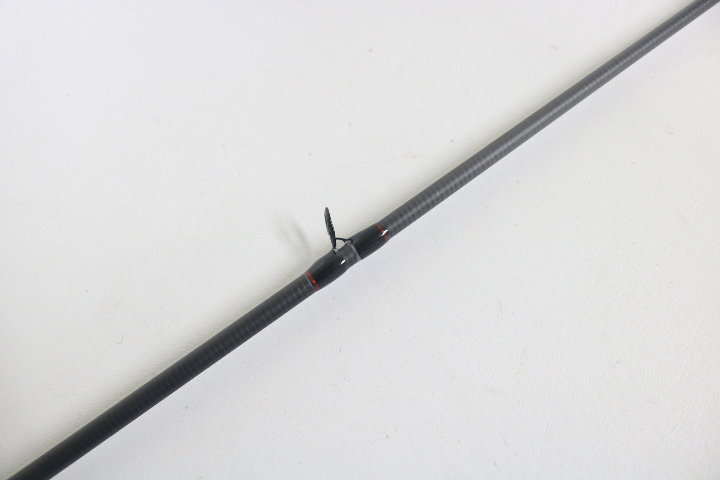 A Dobyns Kaden KD734CB 7'3" Medium Mod-Fast casting rod in excellent used condition rests diagonally on a white surface, featuring a carbon fiber build and a small black fin or propeller-like attachment at its center.