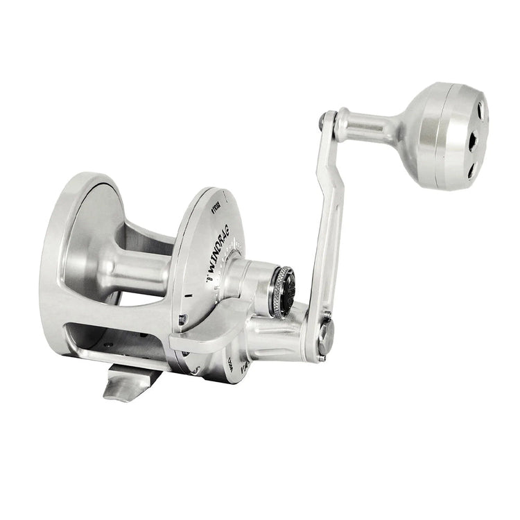 Close-up of a silver fishing reel with a crank handle, designed for use in sport fishing. The metal construction is sleek and shiny, highlighting its modern and sturdy design.