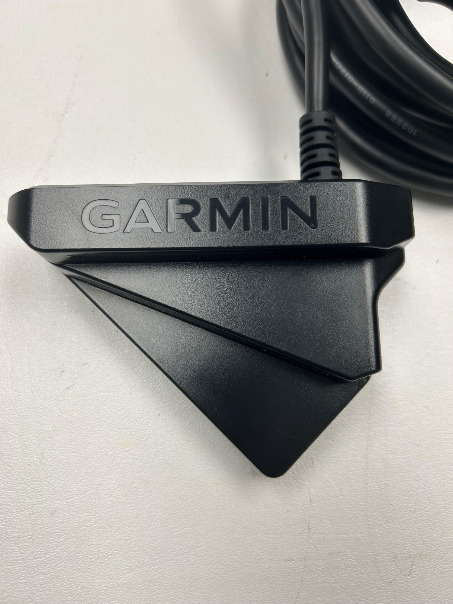 Close-up of a black Garmin transducer with a cable attached, resting on a white surface. The Garmin logo is prominently displayed on the device.