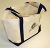 The americanlegacyfishing Fish With Attitude Deluxe Boat Tote Black, a limited edition canvas tote with black handles and trim plus a small Fish With Attitude logo on the front, sits on a light-colored surface.