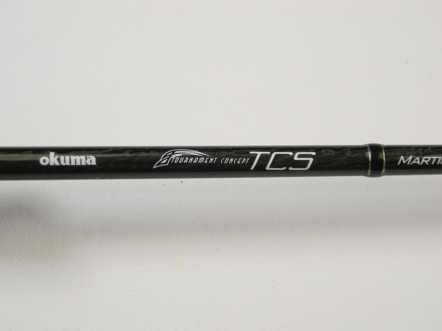 Close-up of a black fishing rod with "Okuma TCS TCS-C-701MH 7'0" Medium Heavy" printed on it against a white background. Ideal for upgrading through our Rod and Reel Trade-In Program, offering store credit on used gear.