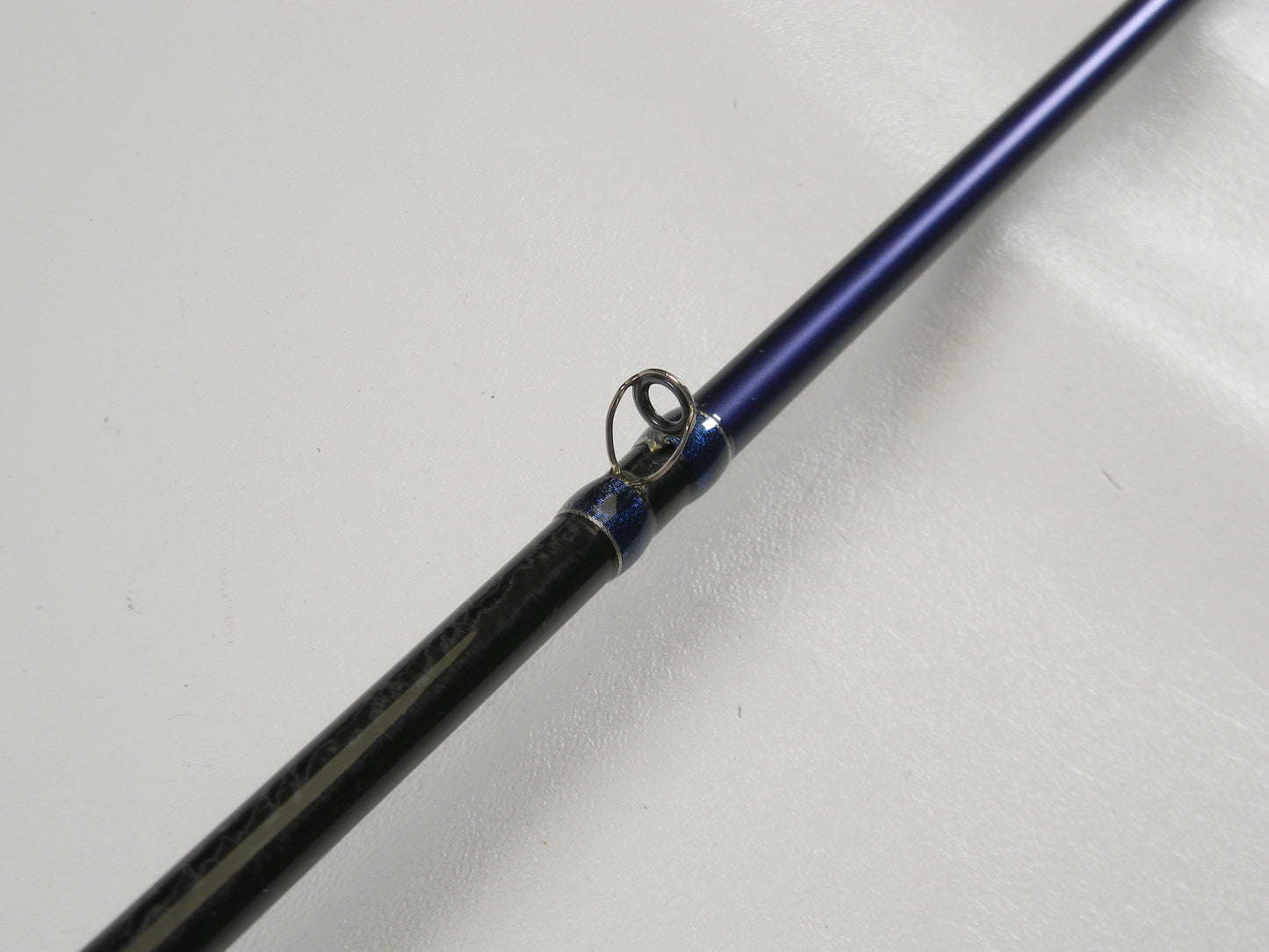 The Okuma TCS TCS-C-701MH 7'0" Medium Heavy Used Casting Rod, in excellent condition, features a close-up of its metal guide ring on a white surface. Trade it in via our Rod and Reel Program to earn store credit or explore quality used gear.