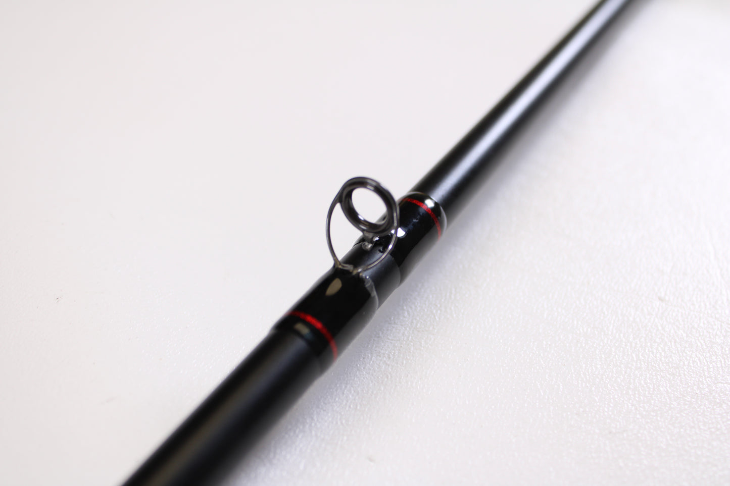 A close-up of the Daiwa DXB DXBT751HRB-G 7'5" Heavy Glass Casting Rod in excellent used condition highlights a line guide, perfect for anglers trading up with our rod and reel program. The black rod with red accents is set against a plain white background.