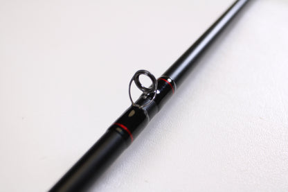 A close-up of the Daiwa DXB DXBT751HRB-G 7'5" Heavy Glass Casting Rod in excellent used condition highlights a line guide, perfect for anglers trading up with our rod and reel program. The black rod with red accents is set against a plain white background.