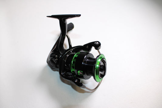 A Dobyns Maverick MV2000 Green spinning reel in mint condition is displayed at an angle on a white surface, highlighting its spool and handle. This used black and green metallic-finish reel showcases the Dobyns brand.