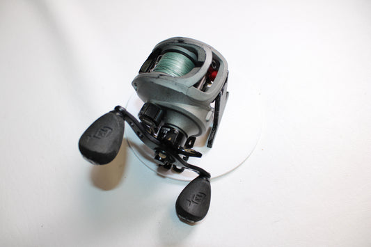 A close-up of the 13 Fishing Inception 6.6:1 Gear Ratio RH used casting reel in fair condition, featuring green line and dual black handles—ideal for those interested in rod and reel trade-ins or quality used gear from 13 Fishing.