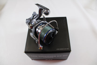 The Daiwa Free Swimmer EX BR 10000 Used Spinning Reel (Excellent Condition) is shown with green line atop a black box—ideal for upgrading via our rod and reel trade-in program.