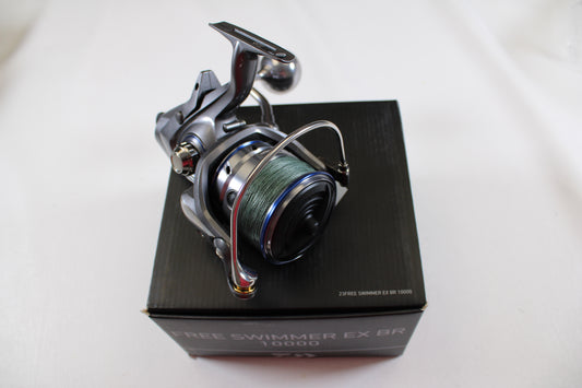 The Daiwa Free Swimmer EX BR 10000 Used Spinning Reel (Excellent Condition) is shown with green line atop a black box—ideal for upgrading via our rod and reel trade-in program.