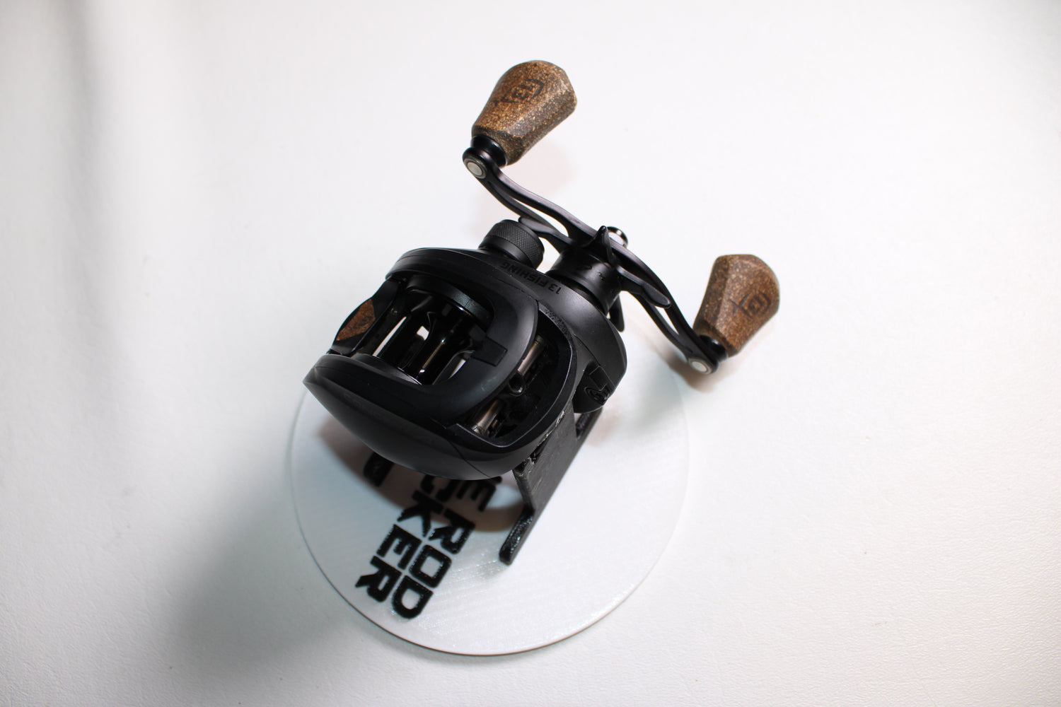 A 13 Fishing Concept A Gen II A2-6.8-LH casting reel in very good used condition, featuring two wooden handle grips, is shown on a white circular surface with partial black text, viewed from above at a slight angle.