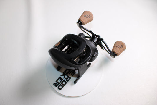 A 13 Fishing Concept A3 Gen II CA3-5.5-LH used casting reel in excellent condition, with cork handles, is shown on a white surface above a round white coaster with black text.