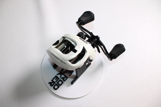 A white 13 Fishing Concept C Gen II C2-6.8-LH casting reel with black handles is displayed on a round white platform with black text, set against a white background.