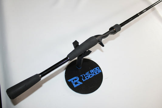 A Daiwa Steez XT STZXT801MHRB used casting rod in good condition, finished in black with a foam grip, rests on a round stand labeled "The Rod Locker" against a plain white background.