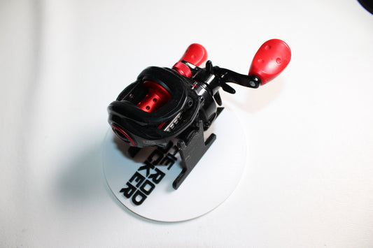 An Abu Garcia MAX4X-L 6.4:1 Gear Ratio LH used casting reel in good condition is displayed on a white round stand labeled "BROKERO," set against a plain white background.