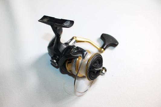 A Shimano Sahara C3000HG-I spinning reel in fair used condition, featuring a black and gold finish, curved handle, and line spool, is displayed on a plain white surface.
