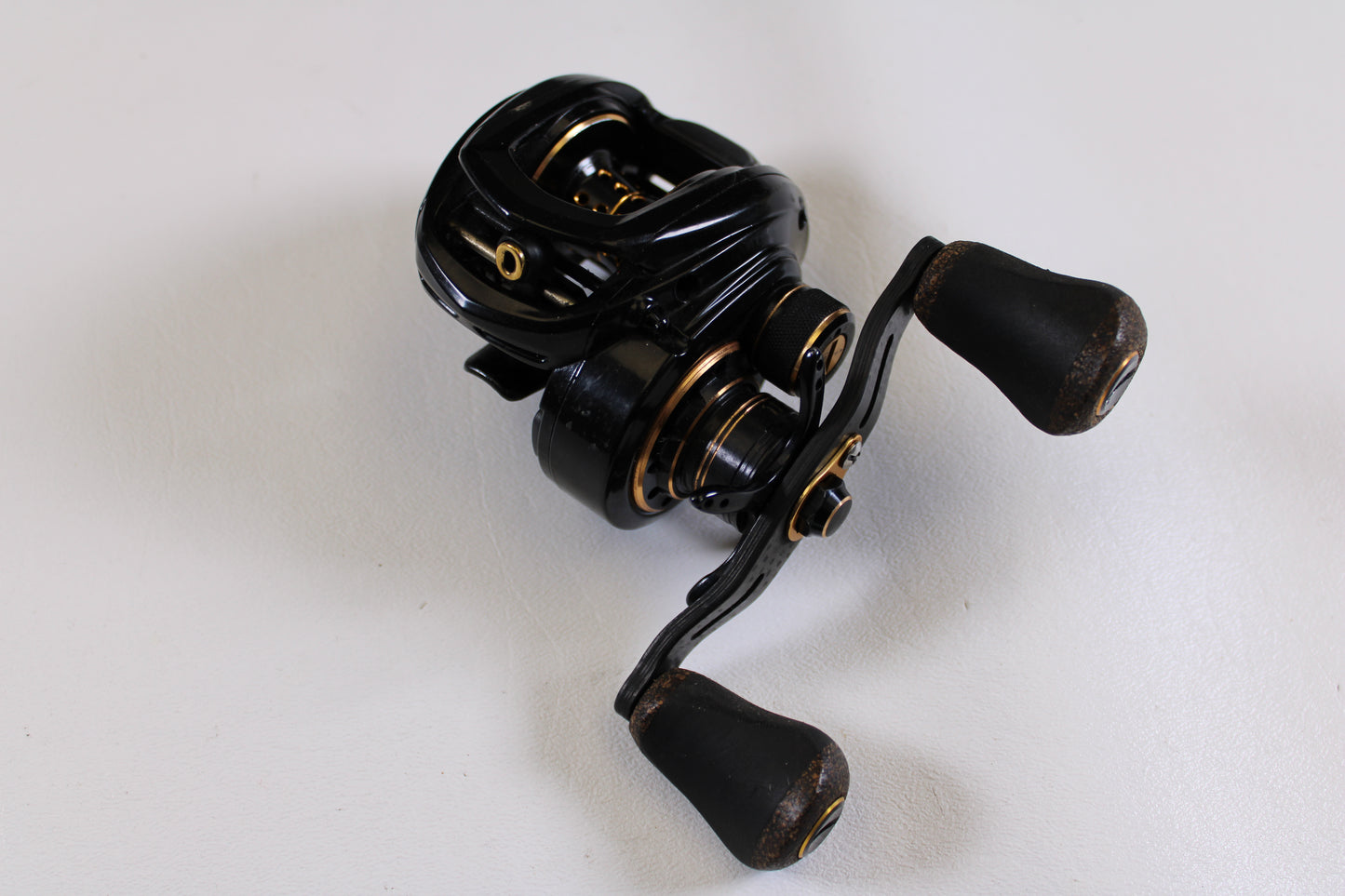 A Lew's Lite MgF LFS 7.5:1 LH used casting reel in good condition, featuring dual handles and a black-and-gold design, rests on a white surface. Trade it in for store credit with our Rod and Reel Trade-In Program.
