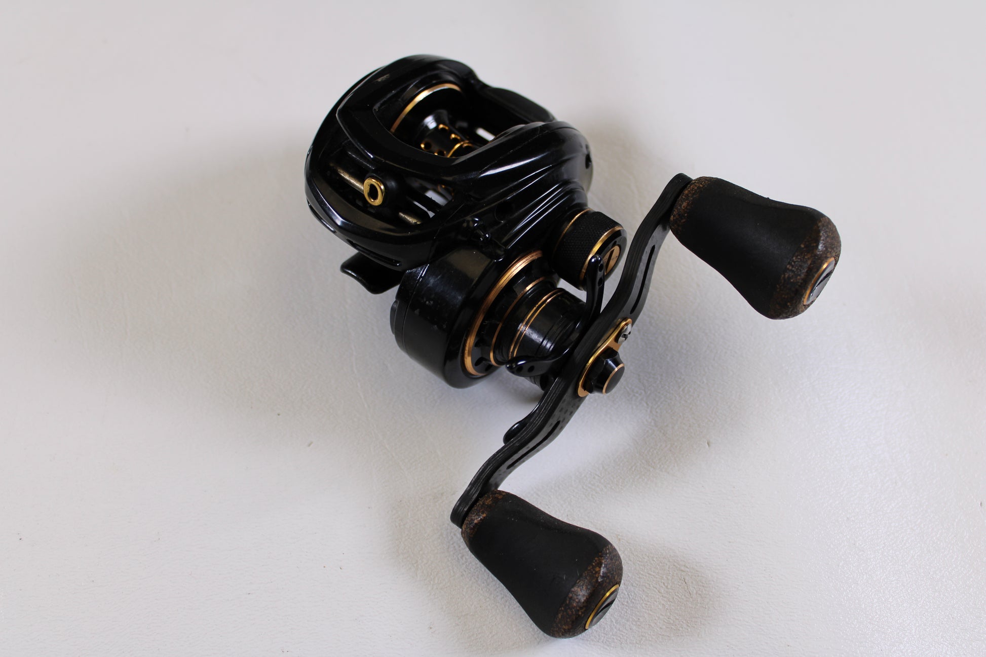 A Lew's Lite MgF LFS 7.5:1 LH used casting reel in good condition, featuring dual handles and a black-and-gold design, rests on a white surface. Trade it in for store credit with our Rod and Reel Trade-In Program.