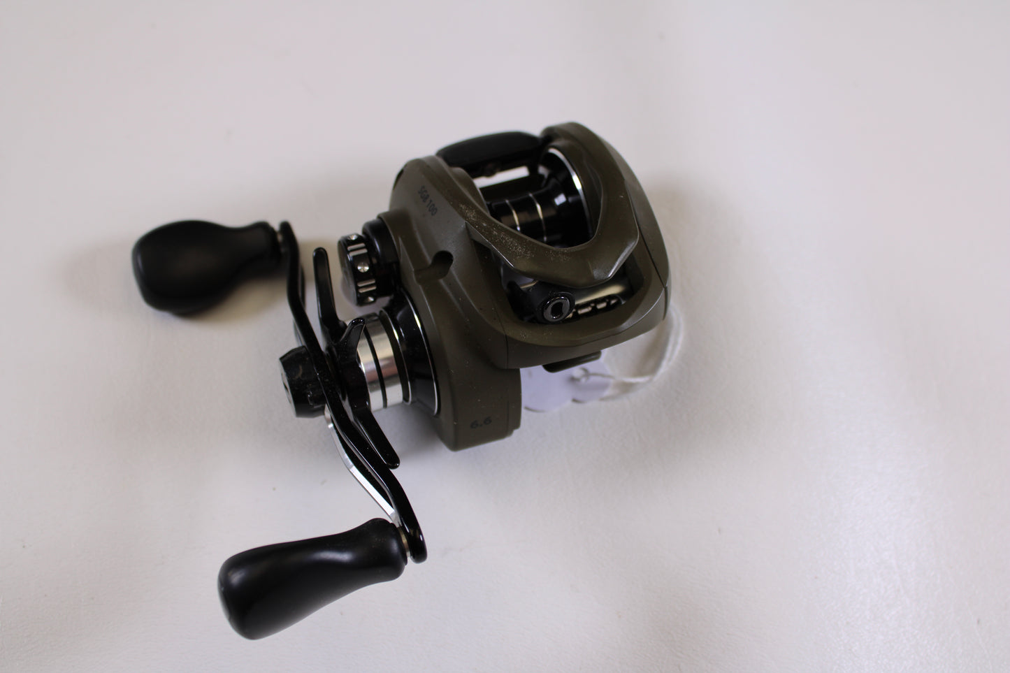 A close-up of a Savage Gear SG8 BC 100 6.6:1 RH - Used Casting Reel in excellent condition, featuring black handles and a greenish-brown body—ideal for earning store credit through our Rod and Reel Trade-In Program.