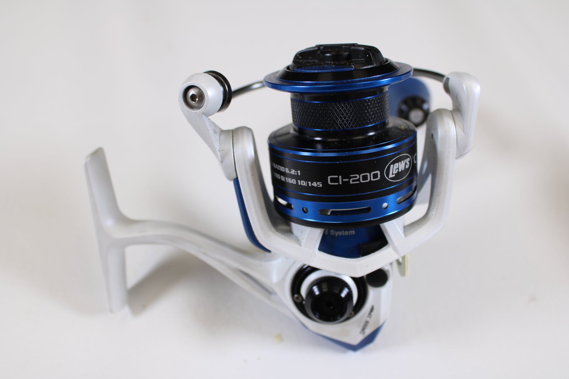 A close-up of a Lew's Custom Inshore CI-200 6.2:1 used spinning reel in good condition, featuring its spool, handle, and bail arm in silver and blue—ideal for anglers seeking quality pre-owned fishing gear.
