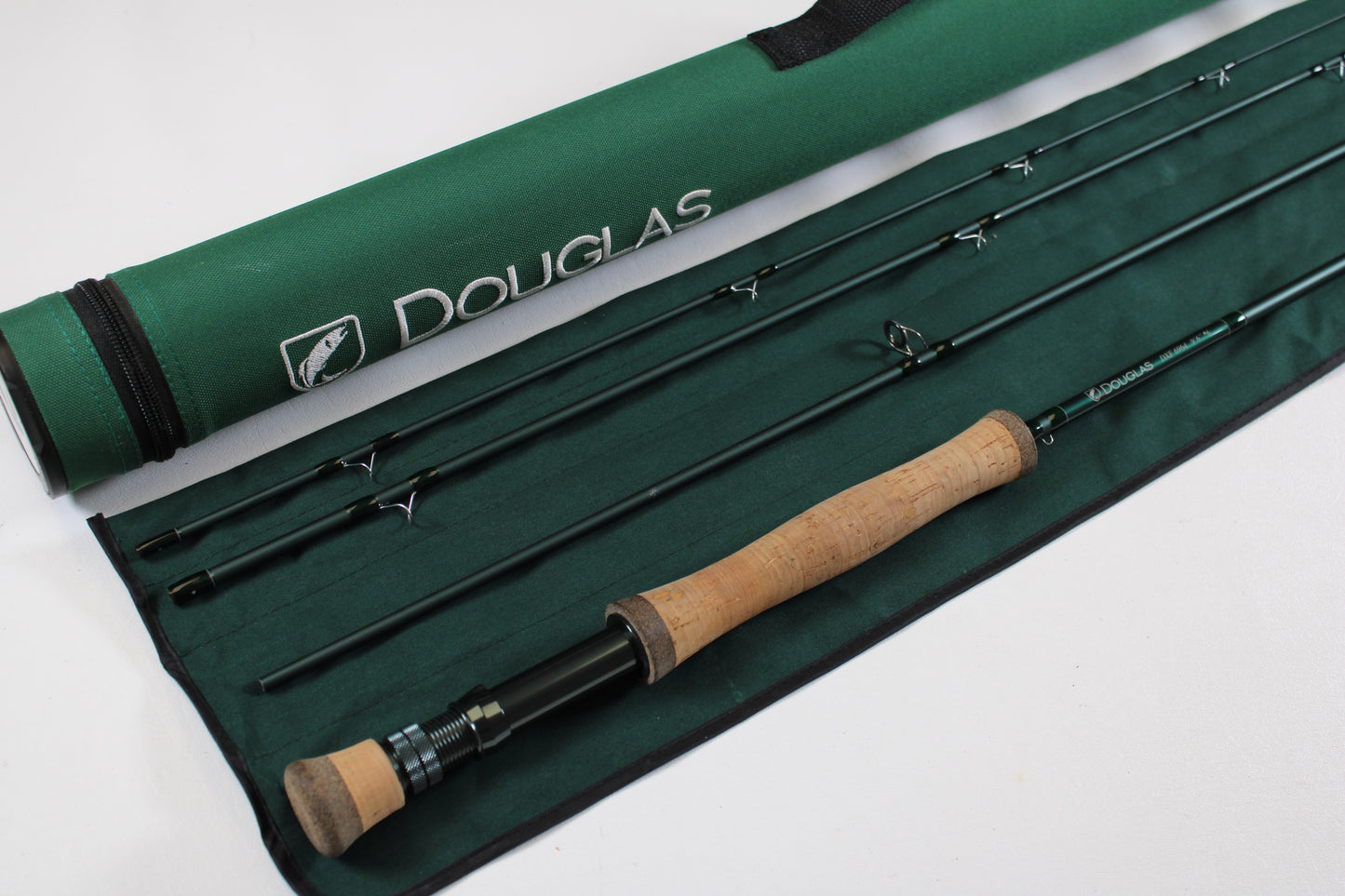 The Douglas DXF Gen 1 6964 9'6" 6wt 4pc Used Fly Rod (Excellent Condition) with cork handle rests on a green case beside a matching Douglas rod tube—ideal for trade-in or as top-quality used gear.