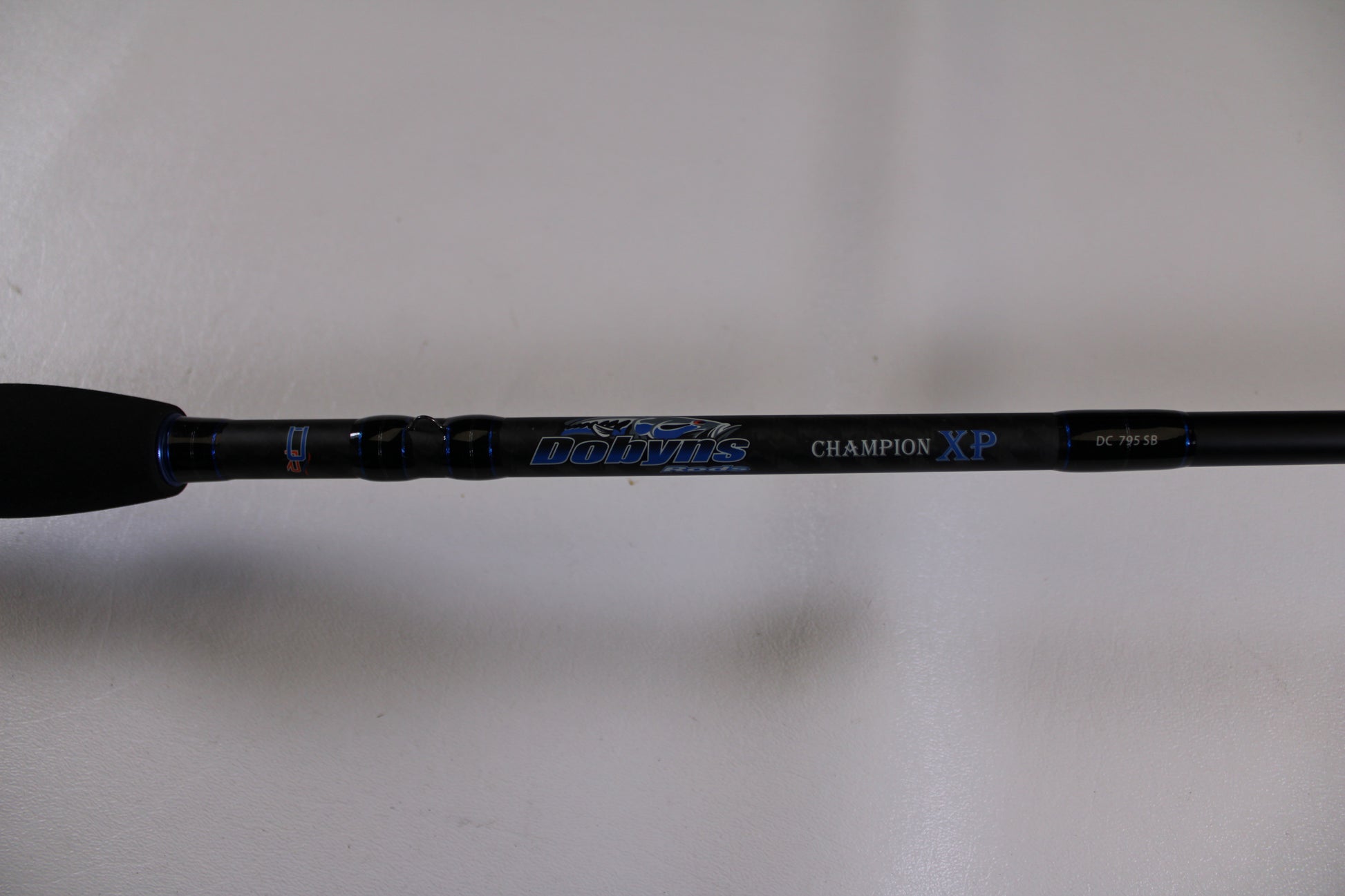 Close-up of a Dobyns Champion XP DC795SB used casting rod handle in excellent condition, featuring blue and silver accents—ideal for our rod and reel trade-in program. Upgrade your fishing gear for store credit. Plain white background.