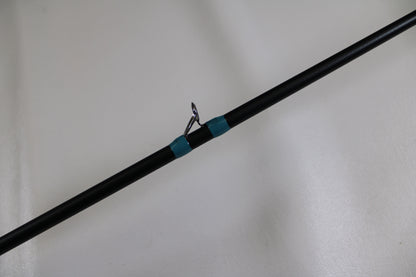 A close-up of the G. Loomis NRX+ 903C MBR Used Casting Rod in excellent condition, featuring a black blank, silver guide ring, and teal thread wrap—eligible for our Rod and Reel Trade-In Program to earn store credit for used gear.
