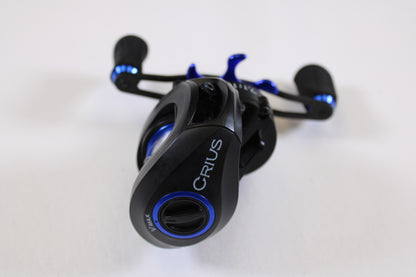 A SixGill Crius 7.1:1 LH used casting reel in excellent condition, black and blue, is displayed on a white background from an angled top-down view—ideal for anglers exploring our rod and reel trade-in program.