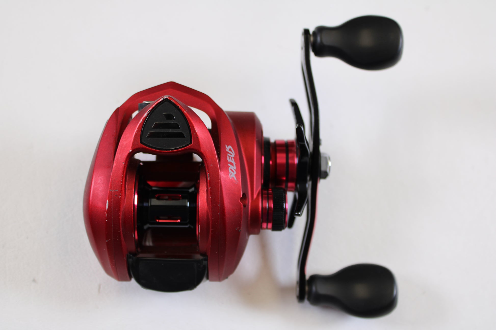 The Favorite Fishing Soleus Red SLSR7R 7.3:1 RH Used Casting Reel (Good Condition) features a red metallic finish and black handles—ideal for upgrading via our Rod and Reel Trade-In Program to earn store credit.