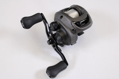 A close-up of a SixGill Arrival Series 6 7.0:1 RH - Used Casting Reel in excellent condition, black and silver with double handle and fishing line—perfect for trading in used gear through our Rod and Reel Trade-In Program for store credit.