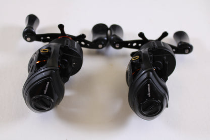 Two used Okuma Citrix Ci-273LXa 7.3:1 LH baitcasting reels in very good condition are side by side on a white surface, showcasing their black finish, handles, and front gears—ideal for rod and reel trade-in or store credit.