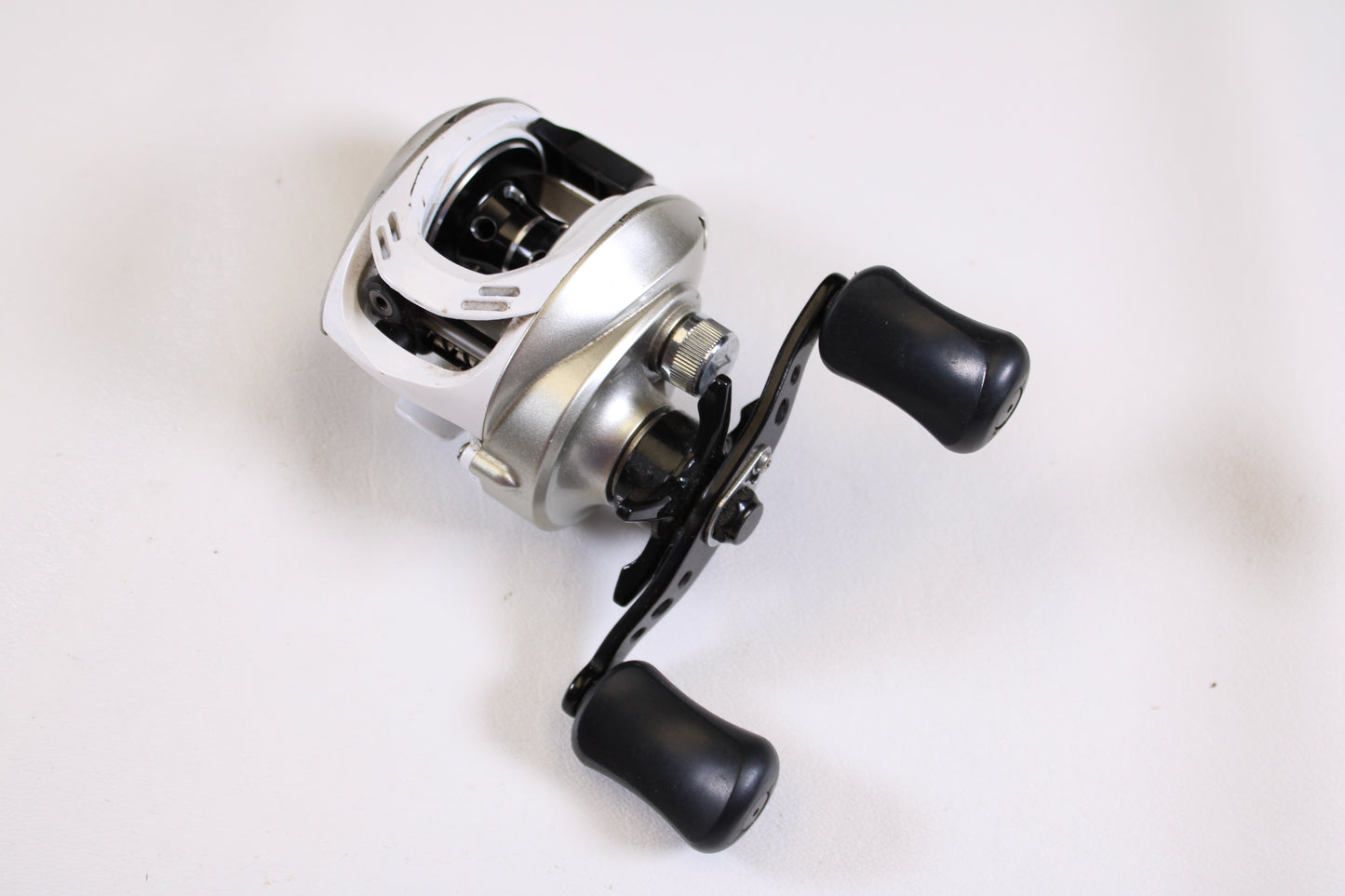 A close-up of the Okuma Stratus V 6.4:1 LH casting reel in good condition, featuring two large black handles on a white background—ideal for upgrading with our rod and reel trade-in program for store credit.