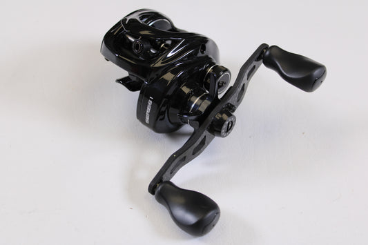 The Kistler Series 1 7.3:1 LH Used Casting Reel in excellent condition features two ergonomic handles and a sleek black design, perfect for rod and reel trade-ins, displayed on a white surface.