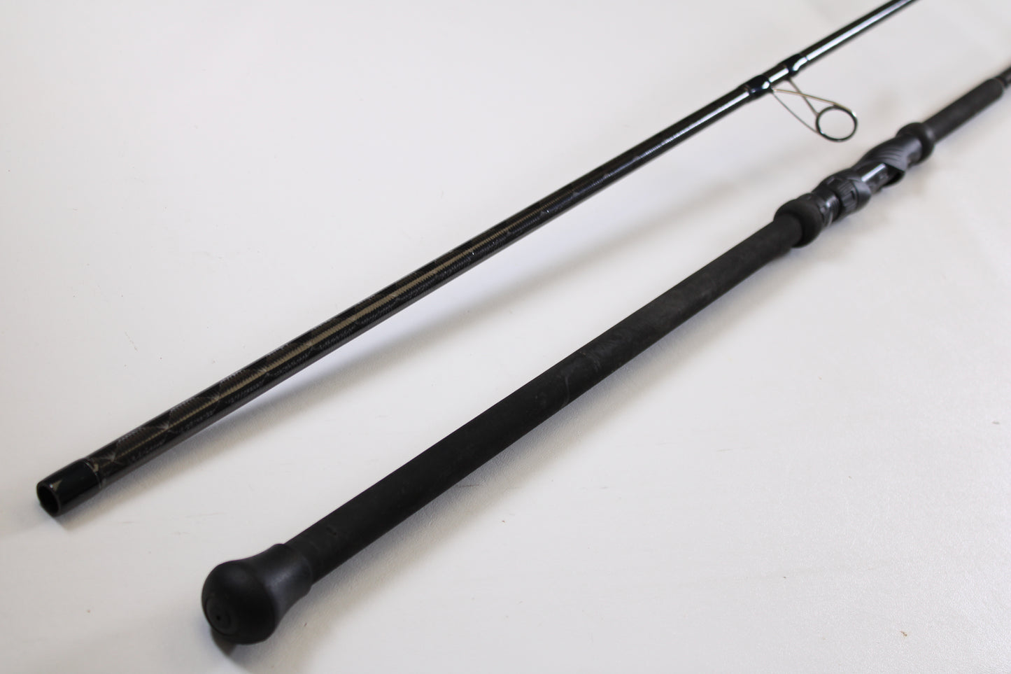 Two black Century SurfMachine SM10L 10'0" 30/70 split used spinning rod sections lie parallel on a white surface. Part of our Rod and Reel Trade-In Program, it includes a handle with reel seat and guide ring—excellent condition.
