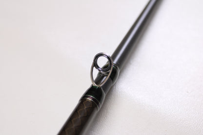 Close-up of a Megabass Orochi XX F6-711XXG Launcher 7'11" used casting rod in excellent condition, highlighting the metal guide ring and textured brown and black handle. Great option for our rod and reel trade-in upgrade program.