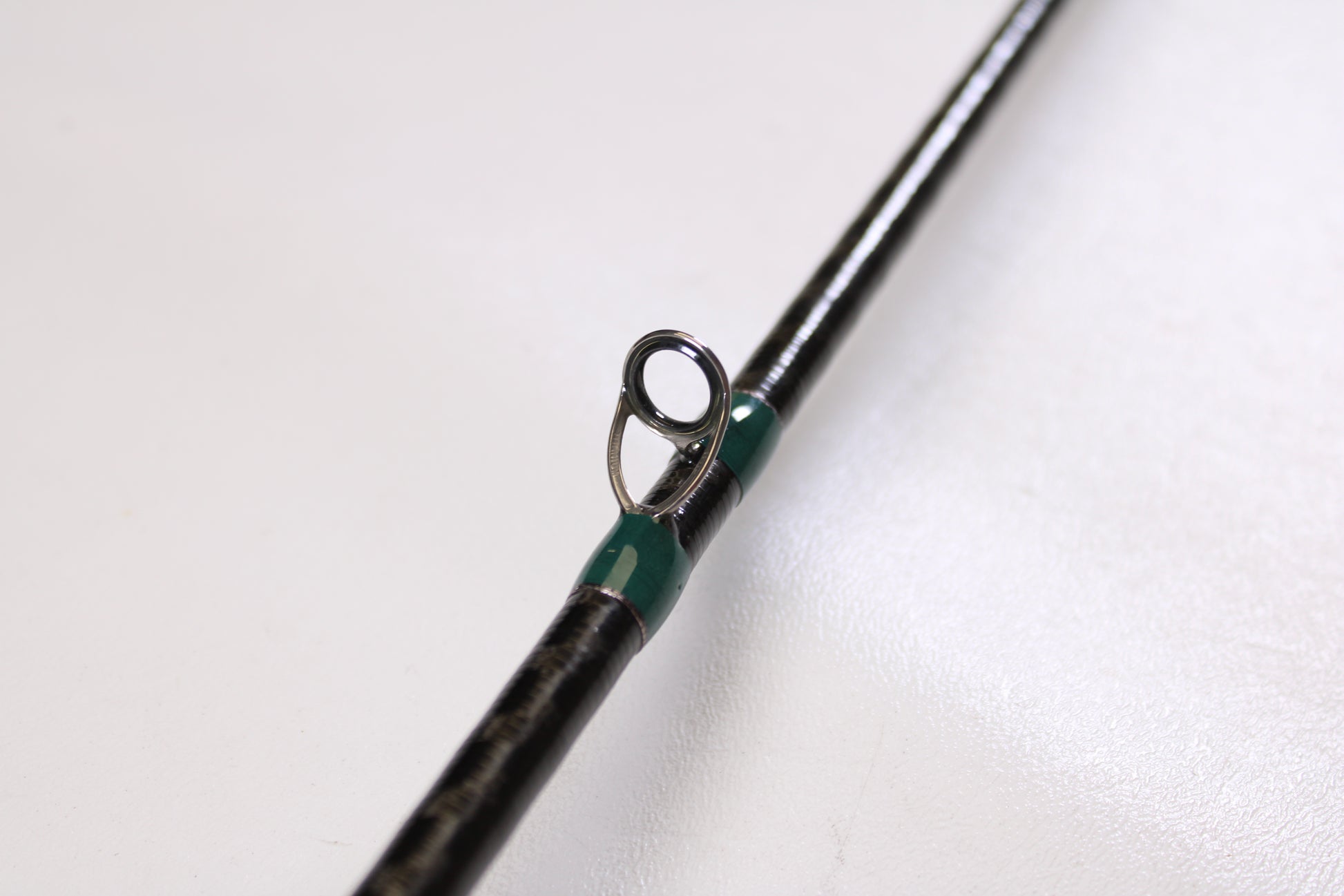 Close-up of a G. Loomis Conquest CNQ 783C MBR 6'6" Medium Heavy Used Casting Rod in excellent condition, featuring a metal guide ring with green thread, perfect for our Rod and Reel Trade-In Program. Shown on a plain white background.